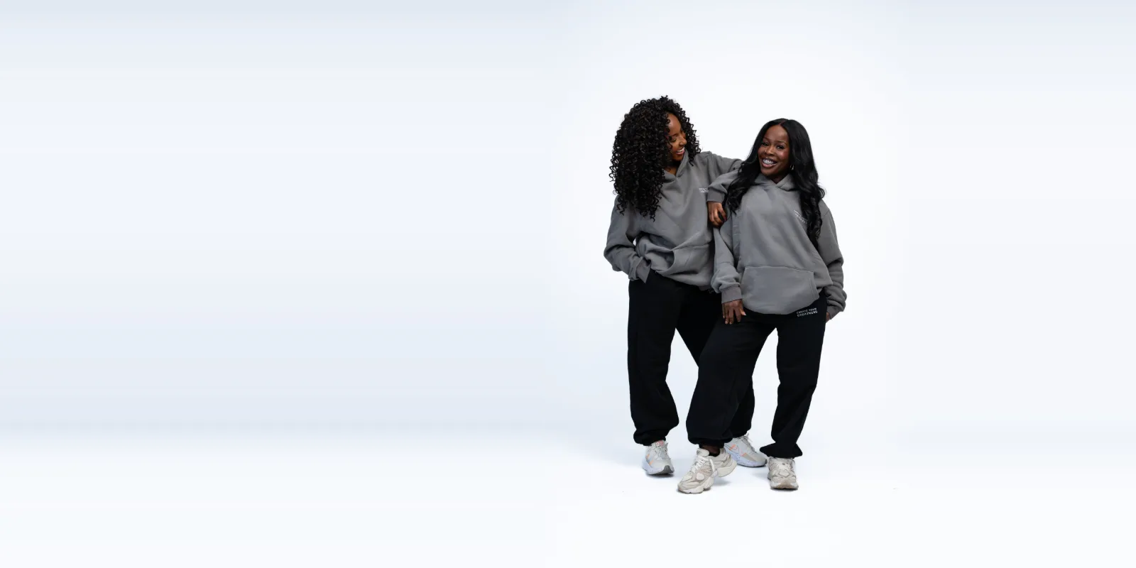 Two women laughing together in grey Signature Hoodies and black Signature Sweatpants